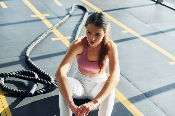 Sitting with rope. Beautiful young woman with slim body type is in the gym. - Photo, Image