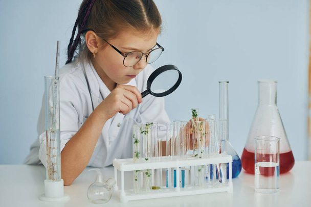 Works with test tubes. Little girl in coat playing a scientist in lab by using equipment. - Foto, immagini