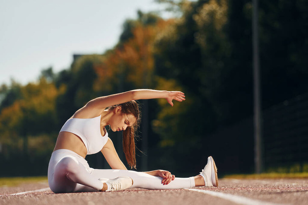 Sitting on the ground. Young woman in sportive clothes is exercising outdoors. - Fotoğraf, Görsel