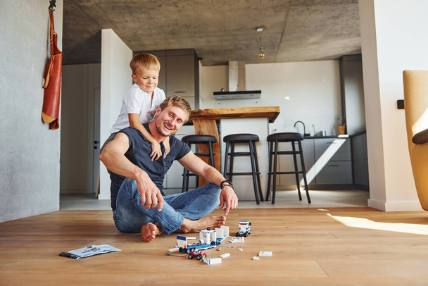 Sitting on the floor and playing with toys. Father and son is indoors at home together. - Fotoğraf, Görsel