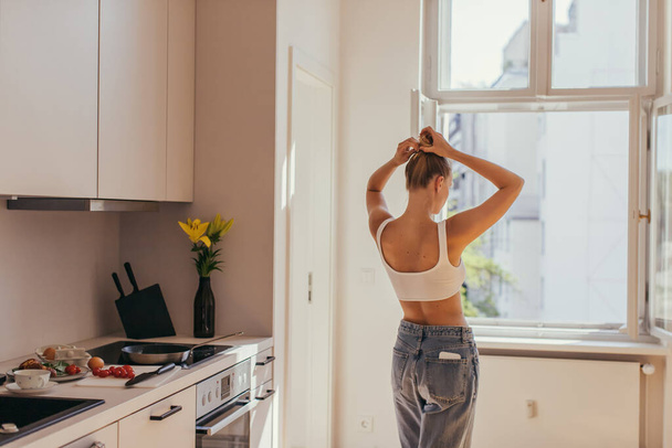 Giovane donna toccare i capelli mentre in piedi in cucina a casa  - Foto, immagini
