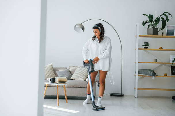 Uses vacuum cleaner. Woman in casual clothes is indoors at home. - Foto, Bild