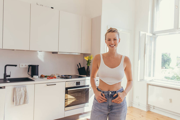 Positive blonde woman in top looking at camera in kitchen  - Fotografie, Obrázek