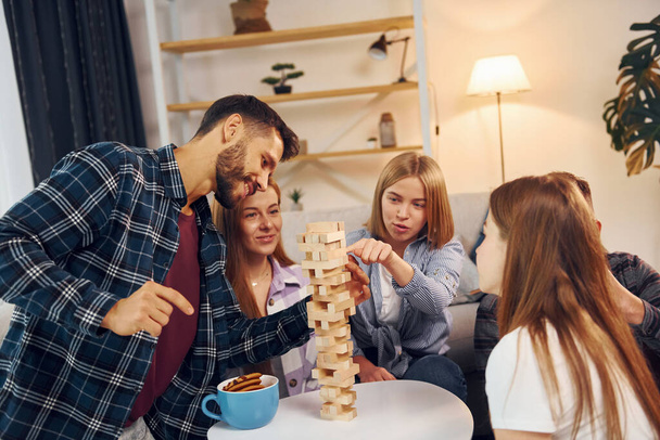 Wooden tower game on the table. Group of friends have party indoors together. - Photo, image