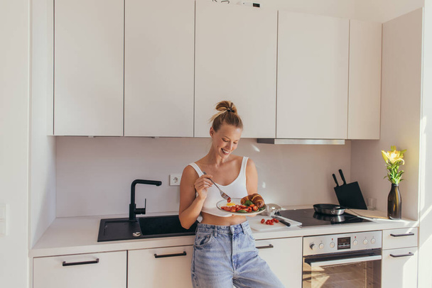 Smiling woman in top holding plate with breakfast in kitchen  - Foto, imagen