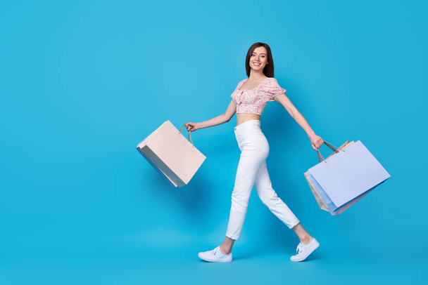 Full length photo of positive pretty carefree lady go empty space carry rejoice purchase stylish outfit isolated on blue color background. - Foto, immagini