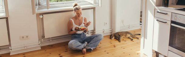 Cheerful woman holding plate with delicious breakfast near scottish fold cat on floor at home, banner  - Fotografie, Obrázek