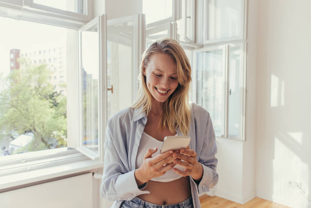 Smiling woman in top and shirt using mobile phone at home  - Foto, immagini