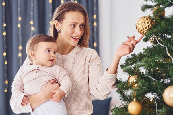 Decorating Christmas tree. Mother with her little daughter is indoors at home together. - Fotoğraf, Görsel