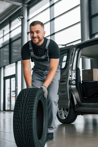 Brand new tire. Man in uniform is working in the autosalon at daytime. - Zdjęcie, obraz