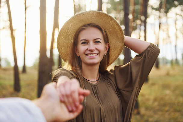 Woman holding man's hand. Happy couple is outdoors in the forest at daytime. - Foto, Imagem