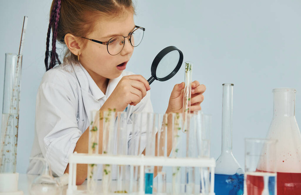 Workes with liquid that is in test tubes. Little girl in coat playing a scientist in lab by using equipment. - Foto, Imagem