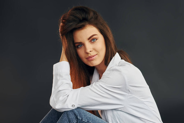 In white shirt and blue jeans. Young beautiful woman is posing for the camera in the studio. - Foto, imagen