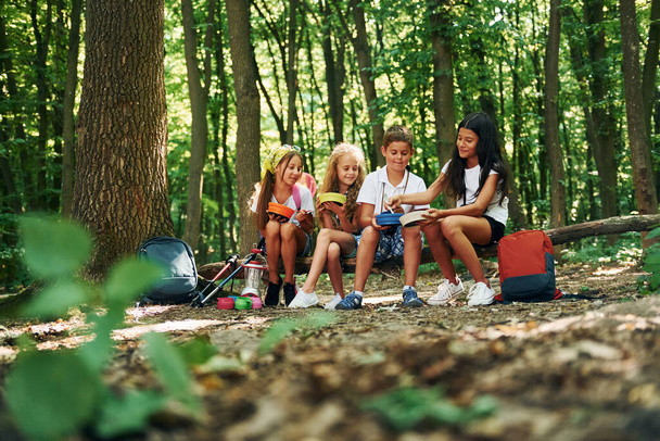 Sitzen und sich ausruhen. Kinder spazieren mit Reiseutensilien im Wald. - Foto, Bild