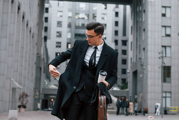 Buildings exterior. Businessman in black suit and tie is outdoors in the city. - Photo, Image