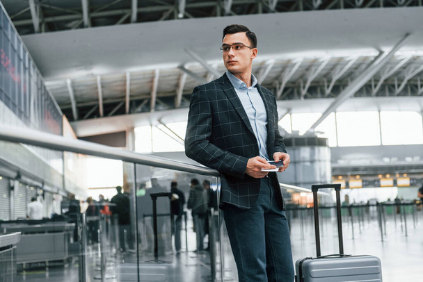 Front view. Young businessman in formal clothes is in the airport at daytime. - Foto, Imagem