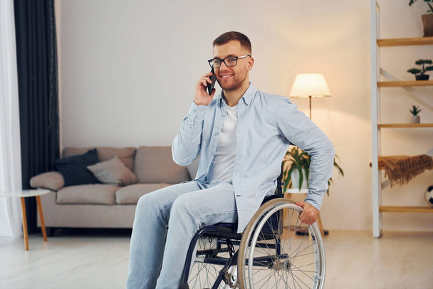 Talking by phone. Disabled man in wheelchair is at home. - Foto, Bild