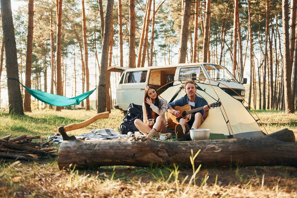 Sitting near the tent. Young couple is traveling in the forest at daytime together. - Foto, Imagen