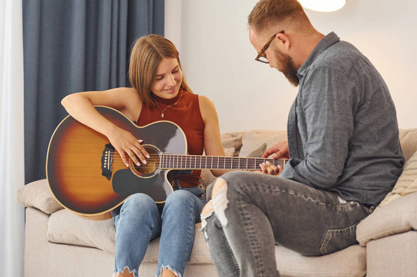 Guitar teacher showing how to play the instrument to young woman. - Fotoğraf, Görsel
