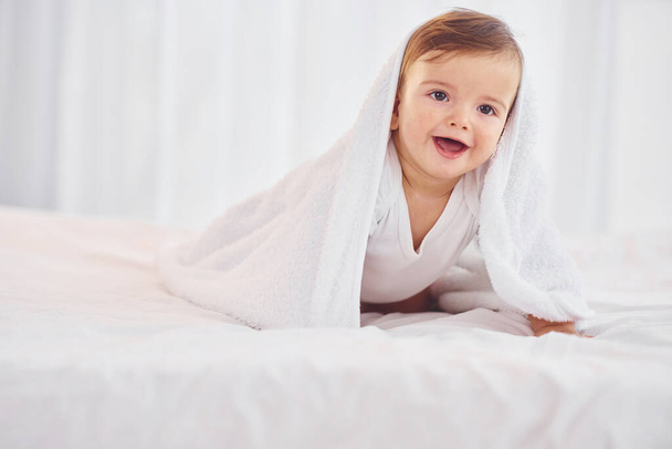 With white towel. Cute little baby is indoors in the domestic room. - Foto, imagen