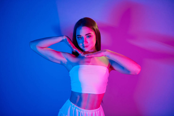 White clothes. Fashionable young woman standing in the studio with neon light. - Zdjęcie, obraz