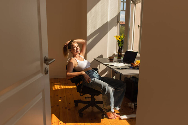Happy barefoot freelancer looking at camera near devices and flowers at home  - Foto, imagen