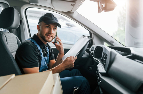 Modern vehicle. Delivery man in uniform is indoors with car and with order. - Foto, Imagem