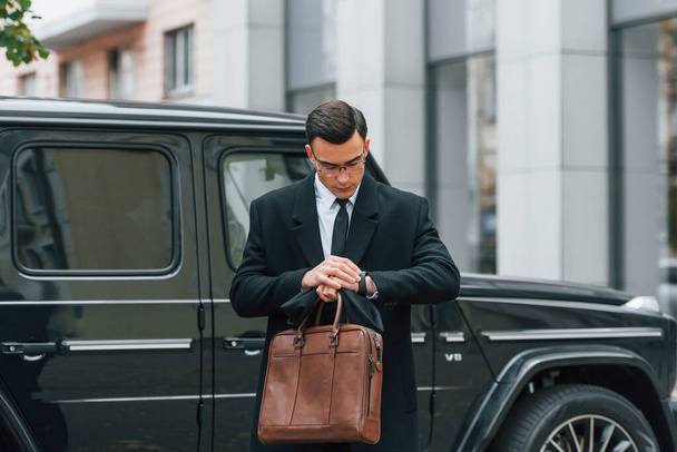 Holding brown bag in hands. Businessman in black suit and tie is outdoors in the city. - Zdjęcie, obraz