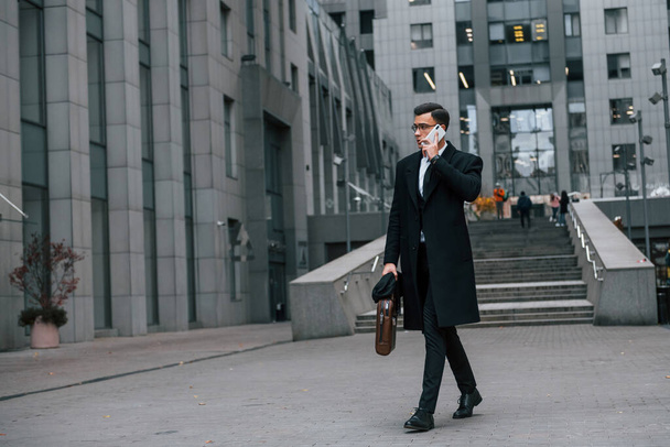 Phone in hand. Businessman in black suit and tie is outdoors in the city. - Valokuva, kuva