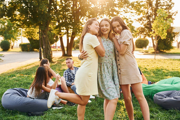 Женщины обнимают друг друга. Группа молодых людей устраивает вечеринку в парке в летнее время. - Фото, изображение