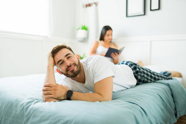 Beau jeune homme en pyjama faire un contact visuel souriant tout en se relaxant lors d'une journée de loisirs en mauvais avec sa femme ou sa petite amie - Photo, image
