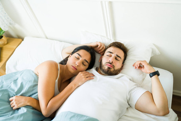 Αναστατωμένος καυκάσιος άντρας που ξυπνάει στο κρεβάτι με μια γυναίκα που αγκαλιάζεται και νιώθει άβολα μετά το σεξ.  - Φωτογραφία, εικόνα
