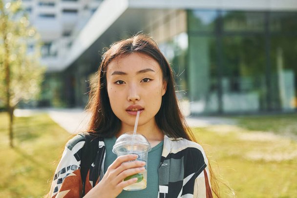 With fresh drink. Young asian woman is outdoors at daytime. - Fotografie, Obrázek