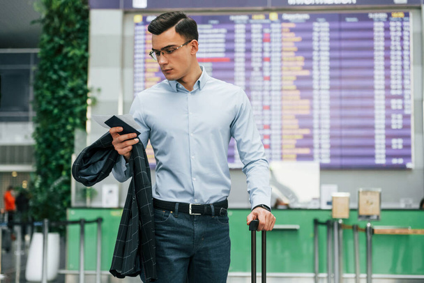 Holding phone. Young businessman in formal clothes is in the airport at daytime. - Photo, image