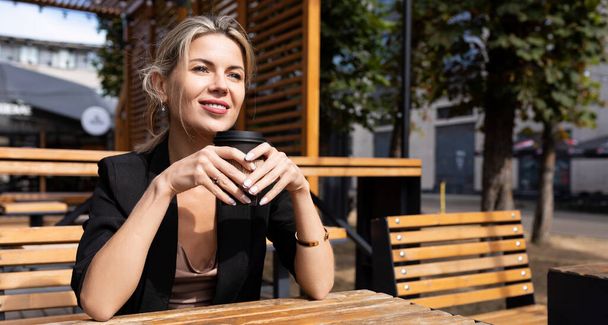ストリートカフェでコーヒーを飲む自信のあるビジネス女性が顔に笑顔で. - 写真・画像