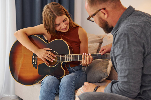 Private lesson. Guitar teacher showing how to play the instrument to young woman. - Fotó, kép