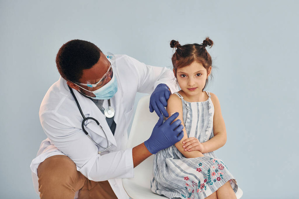 Młody, afrykański lekarz wstrzykujący małej dziewczynce w szpitalu.. - Zdjęcie, obraz