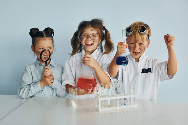 Счастливые друзья улыбаются. Дети в белых халатах играют ученых в лаборатории с помощью оборудования. - Фото, изображение