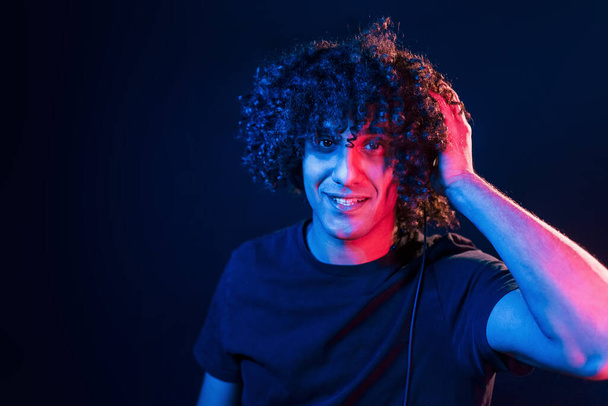 Young DJ with curly hair standing in the club with neon light. - Foto, immagini