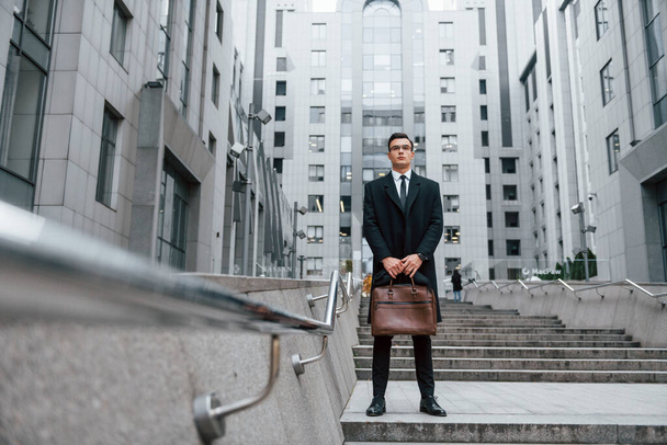 Buildings exterior. Businessman in black suit and tie is outdoors in the city. - 写真・画像