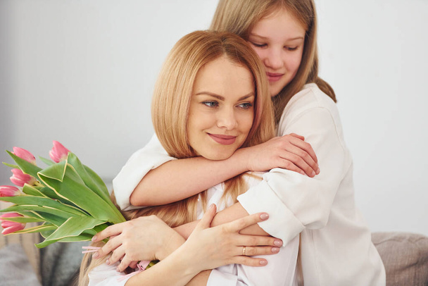 Girls gives flowers. Young woman with her daughter is at home at daytime. - Fotoğraf, Görsel