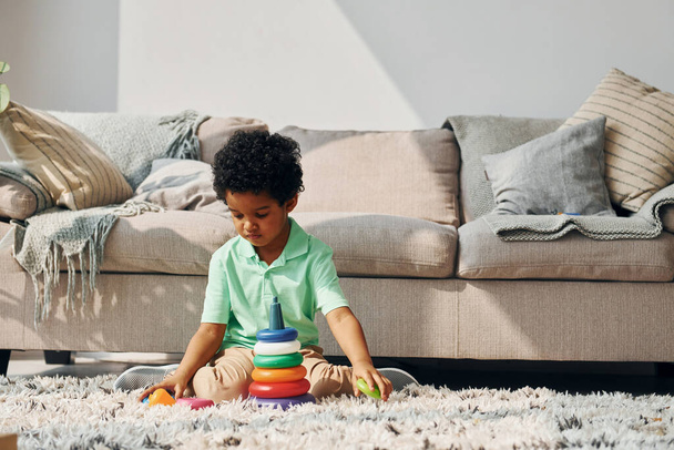 Afrikkalainen amerikkalainen lapsi leikkii leluilla sisätiloissa sängyn lähellä kotona. - Valokuva, kuva