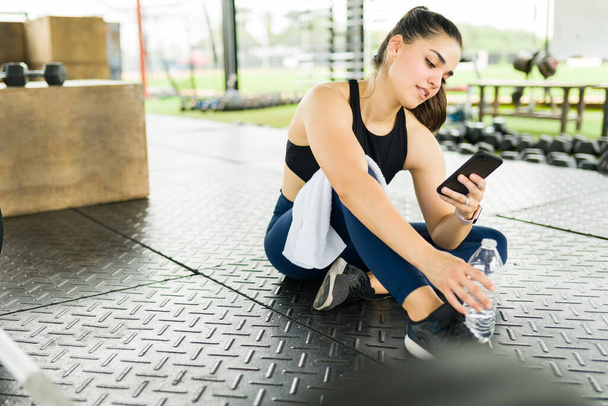 Красива підходить молода жінка смс на смартфоні з друзями, приходячи в спортзал, щоб зробити її тренування вправи
 - Фото, зображення
