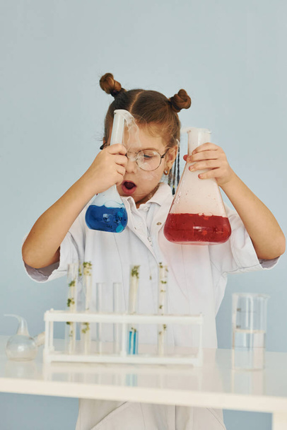 Scared little girl in coat playing a scientist in lab by using equipment. - Foto, afbeelding