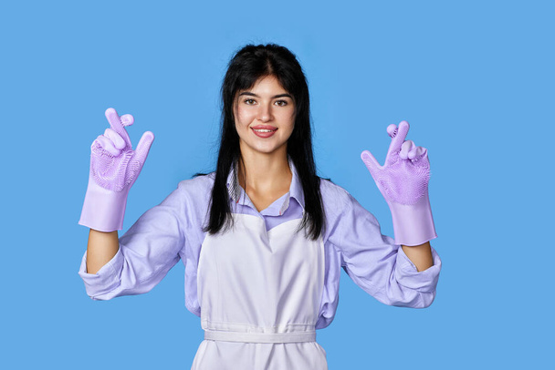 caucasian woman in rubber gloves with finger crossed gesture isolated on blue background. cleaning - Fotoğraf, Görsel