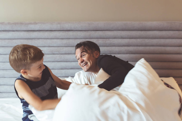 Szczęśliwy ojciec i syn bawią się podczas zabawy na łóżku.  - Zdjęcie, obraz