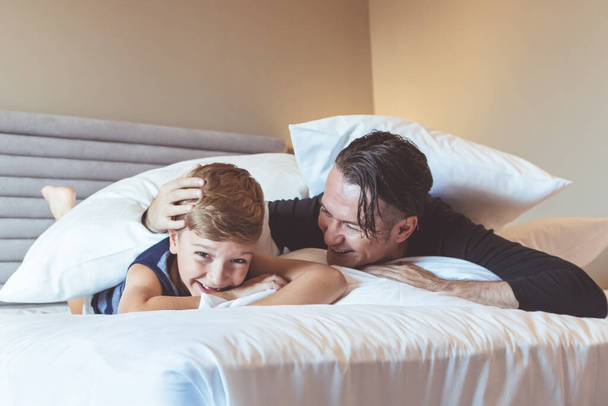 Feliz padre e hijo riendo mientras se divierten en el dormitorio.  - Foto, Imagen