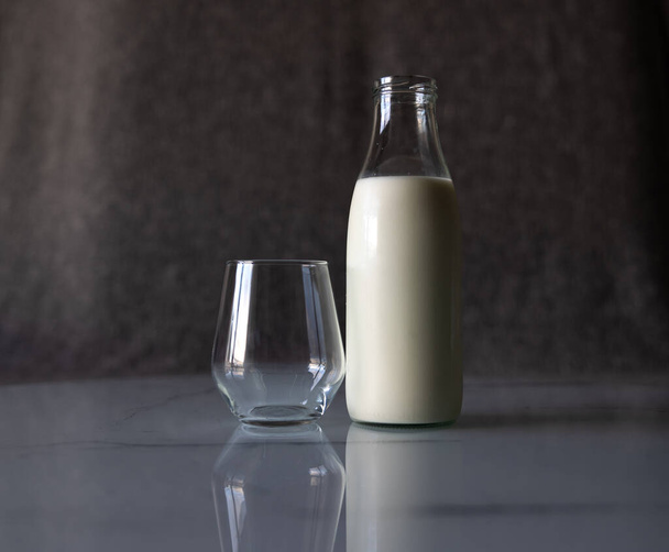 An empty glass is on the table next to a full bottle of milk. High quality photo - Foto, afbeelding