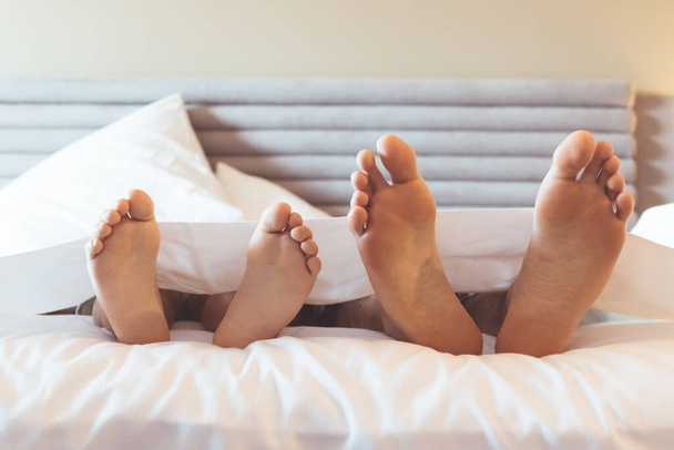 Feet of father and kid lying down on the covered with bed sheet. - Fotoğraf, Görsel