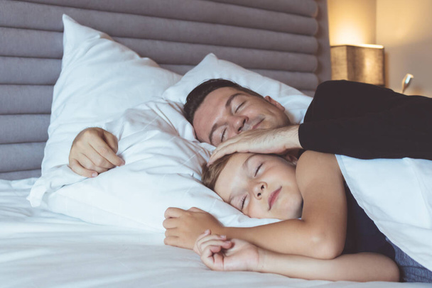 Zorgzame vader en zijn zoon slapen samen in de slaapkamer.  - Foto, afbeelding